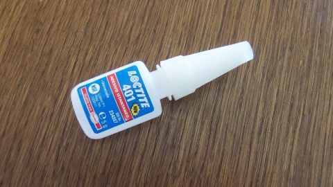 Eine Flasche Sekundenkleber liegt auf einem Holztisch, bereit, zum Entfernen mit Aceton verwendet zu werden.
