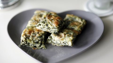 Auf einem herzförmigen Teller liegen mehrere Stücke einer leicht gebackenen Spinatlasagne, appetitlich angerichtet.