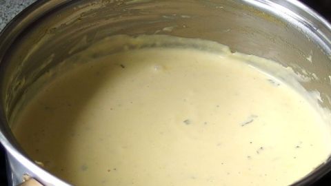 Eine cremige Sauce Hollandaise köchelt in einem Topf auf dem Herd, umgeben von einer küchenähnlichen Umgebung.
