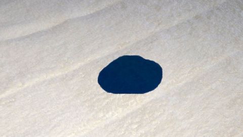 Ein blauer Tintenfleck liegt auf einem hellen, glatten Untergrund und deutet auf mögliche Verschmutzung hin.