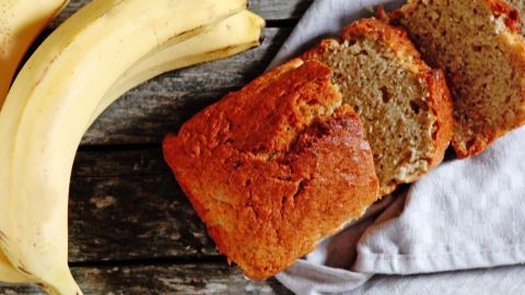 Ein goldbrauner Bananen-Napfkuchen liegt auf einem Handtuch, während frische Bananen daneben ruhen.