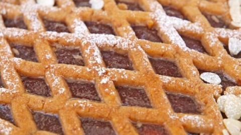 Linzer Torte zeigt ein Gittermuster, bedeckt mit Puderzucker und Mandelscheiben, auf einer dunklen Fruchtfüllung.