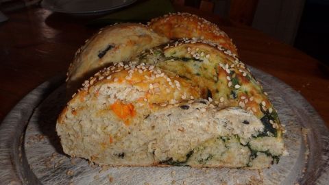 Ein Hefezopf mit würzigen Füllungen liegt auf einem Holzbrett, leicht angeschnitten und mit Sesam bestreut.