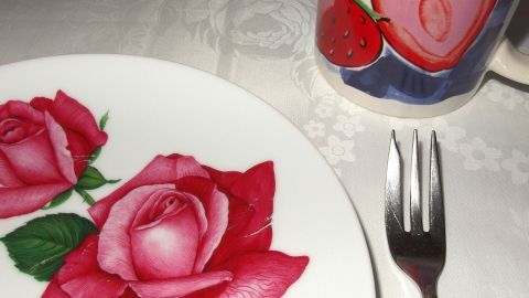 Eine bunte Gästetasse und ein Teller mit essbaren Rosen schmücken den gedeckten Tisch für Kinder.
