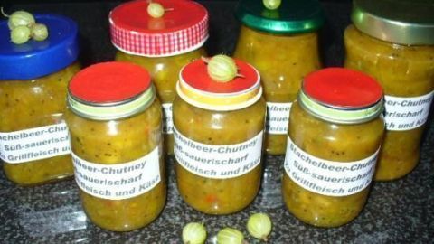 Glasbehälter mit feurig scharfem Stachelbeer-Chutney stehen auf einer dunklen Oberfläche, dekoriert mit Stachelbeeren.