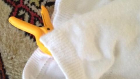 Weiße Socke mit gelber Wäscheklammer am Saum befestigt, auf einem gemusterten Teppich liegend.