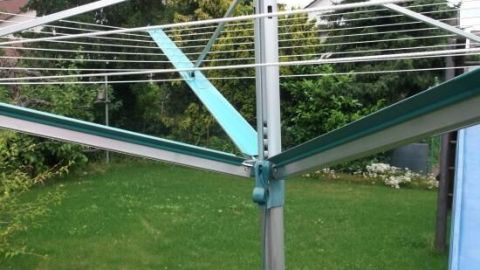 Eine Wäschespinne steht in einem grünen Garten, die Leinenautomatik wirkt schwergängig und benötigt möglicherweise Wartung.