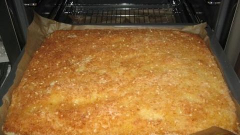 Ein frisch gebackener Kokos-Mandel-Kuchen liegt auf einem Blech, während er in einem leicht offenen Ofen steht.