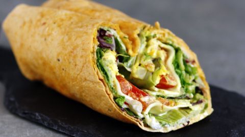 Ein leckerer Wrap liegt auf einem schwarzen Steinbrett, gefüllt mit frischem Gemüse und einer goldenen Tortilla.