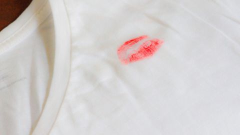 Ein weißes T-Shirt liegt flach auf einem Tisch und zeigt einen roten Lippenstiftfleck, der wie ein Lippenabdruck aussieht.