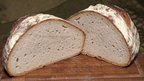 Ein frisch gebackenes Roggenmischbrot ohne Sauerteig liegt auf einem Holzbrett, das Brot ist aufgeschnitten und zeigt die saftige Krume.