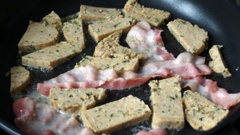 Reste von Knödeln am nächsten Tag in der Pfanne anbraten. Gekochte Knödel liegen in einer Pfanne, während sie mit Speck angebraten werden, um ein herzhaftes Gericht zu kreieren.