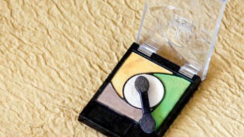 Ein Lidschatten-Set mit vier Farben liegt offen auf einer gelben, strukturierten Oberfläche, bereit zur Anwendung für intensivere Farben.