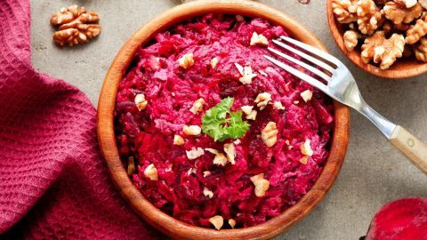 Ein kräftig roter Rote-Bete-Salat wird in einer Holzschüssel serviert, garniert mit Walnüssen und frischem Grün.