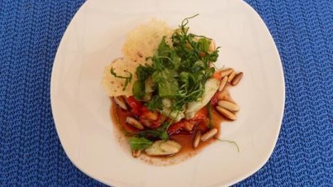 Ein Teller mit Erdbeersalat, garniert mit frittiertem Rucola und Mandeln, auf einem blauen Tisch.