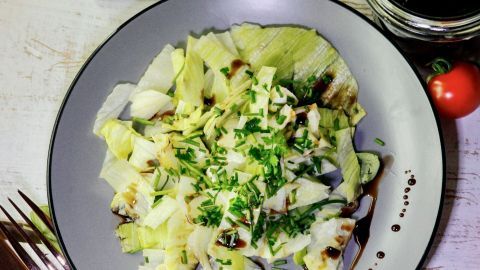 Ein frischer, grüner Salat mit einer cremigen Salatdressing-Soße wird auf einem grauen Teller serviert, umgeben von Besteck.