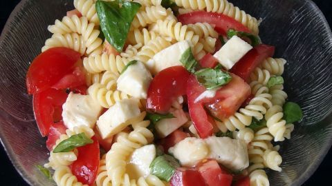 Eine Schüssel Pasta mit Tomaten und Mozzarella mischt frische Zutaten und zeigt eine bunte, sommerliche Mahlzeit.