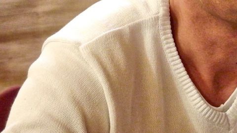 Ein weißer Wollpullover liegt auf einem Tisch, während eine Person ihn sanft und sorgfältig behandelt.