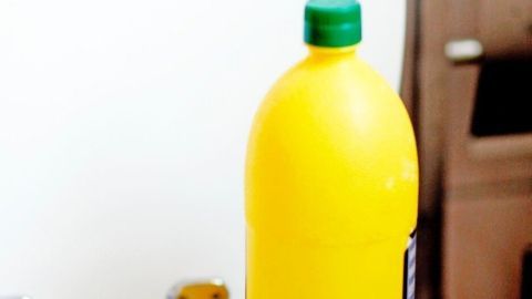 Eine gelbe Flasche mit grünem Deckel steht auf dem WC-Sitz und deutet auf das Putzen mit Zitronensäure hin.