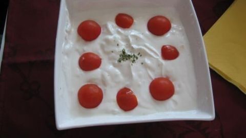 Eine weiße Schüssel mit Zwiebelschmand, garniert mit Kirschtomaten und Kräutern, steht auf einem dunklen Tischtuch.