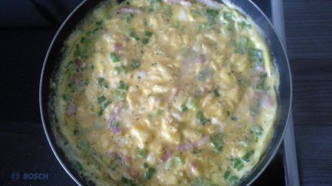 Für ein cremigeres Omelette einfach Sahne statt Milch verwenden. Das Bild zeigt ein leckeres Omelette mit frischen Frühlingszwiebeln und Schinkenstreifen in der Pfanne. So wird das Frühstück ein Genuss! Omelette in einer Pfanne auf einem Herd, mit Frühlingszwiebeln und Schinkenstückchen garend. Text: "BOSCH".