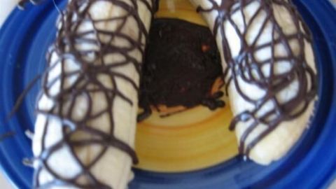 Bananen auf einem blauen Teller, überzogen mit Schokoladensoße, bilden eine süße, kreative Präsentation.