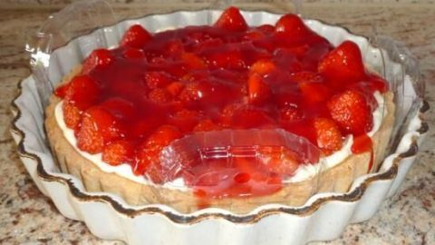 Erdbeerkuchen steht in einer geriffelten Keramikform und ist mit einer durchsichtigen Plastikkuppel vor Beschädigung geschützt.