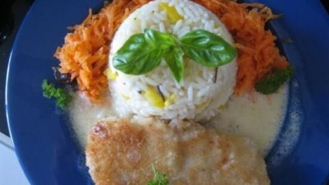 Knuspriger Kabeljau liegt neben Paprikareis mit Basilikum auf Sahnesauce, umgeben von geraspeltem Möhrensalat auf blauem Teller.