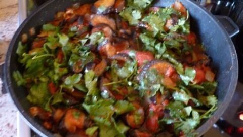 Eine Pfanne mit frischen, gehackten Auberginen, Tomaten und Koriander, die auf dem Herd köchelt.