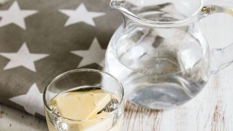 Ein durchsichtiges Glas mit Butterwürfel steht neben einer Glaskaraffe mit Wasser auf einem Tisch mit einem Sternen-Tuch.