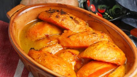 Kandierte Süßkartoffeln liegen in einer braunen Schüssel, umgeben von einer roten Tischdecke und frischen Süßkartoffeln.