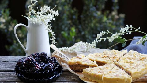 Kekse mit Mandeln liegen auf einem rustikalen Holztisch, umgeben von frischen Brombeeren und floralen Dekorationen.