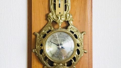Ein antikes Thermometer und Barometer hängen an einer Holzplatte, die die Raumtemperatur und den Luftdruck anzeigt.