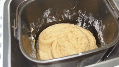 Eine helle, geschmeidige Hefeteigmasse ruht in der Backform eines Brotbackautomaten und wartet auf die Zubereitung.