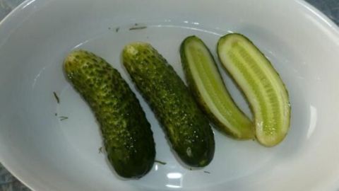 Gurken liegen in einer weißen Schale; zwei sind ganz, eine ist längs halbiert, um die saftige grüne Mitte zu zeigen.