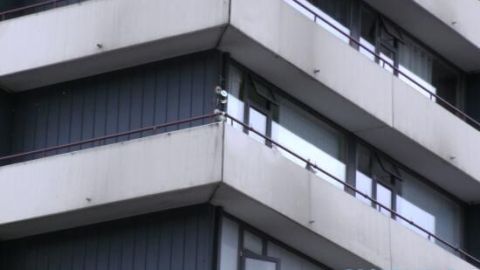Balkon mit Fenstern in einem Gebäude, wo CDs aufgehängt sind, um Stadttauben abzuhalten. Baustellenarchitektur im Hintergrund.
