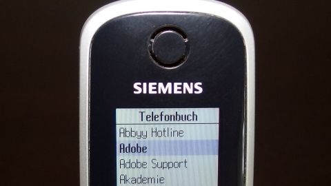 Ein Schnurlostelefon zeigt ein Menü mit Optionen wie "Telefonbuch" und "Rückruf Hotline" in einem dunklen Raum.