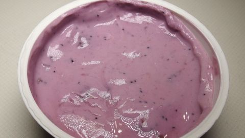 Ein Becher mit cremigem Fruchtjoghurt ohne Sägespäne und Zellstoff steht auf einem neutralen Hintergrund.