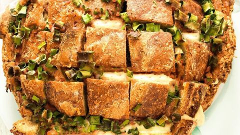 Ein rustikales Pull-away-Brot mit bequemer Aufteilung, garniert mit frischem Schnittlauch auf einem weißen Teller.