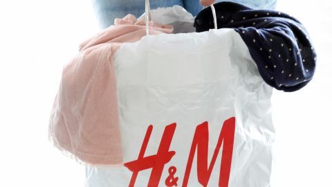 Eine Person hält eine Einkaufstüte von H&M mit alten Klamotten, bereit, diese gegen Rabatt einzutauschen.