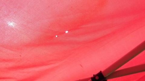 Ein rotes Pavillon-Dach zeigt zwei kleine Löcher, durch die Lichtstrahlen scheinen, es stehen keine Wasseransammlungen sichtbar.