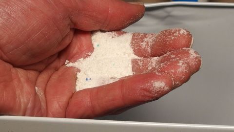 In einer Hand liegt Waschpulver, während es in einen Behälter gegossen wird, um als Handwaschpaste verwendet zu werden.