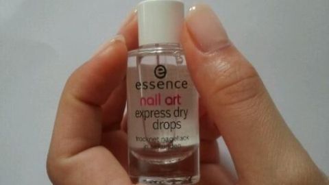 Eine Hand hält eine kleine Flasche mit Pipette. Auf dem Etikett steht: "essence nail art express dry drops trocknet nagellack".
