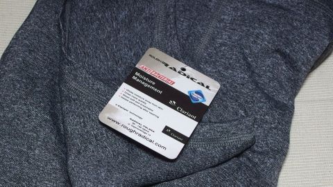 Ein graues Sport-Shirt liegt auf einem hellen Untergrund, mit einem Etikett, das Informationen über das Produkt enthält.