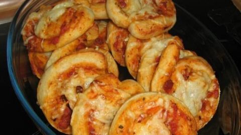Pizzaschnecken liegen gebacken in einer Glasform, bedeckt mit reichlich Käse, in einer heimischen Küchenumgebung.