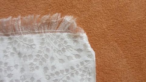 Ein Schal mit handgemachten Fransen liegt auf einem orangefarbenen Untergrund und zeigt kunstvoll bearbeiten Ränder.