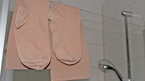 Kompressionsstrümpfe hängen an einer Duschstange, während der Duschkopf im Hintergrund sichtbar ist.
