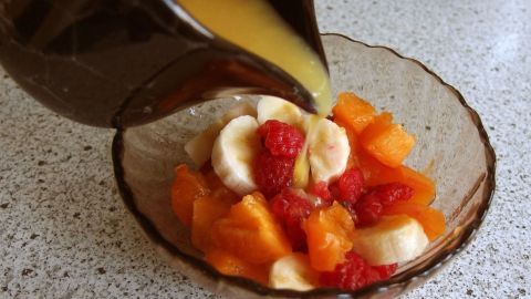 Ein Glas mit frischem Obstsalat wird mit einer süßen Sauce übergossen, auf einer hellen Küchenarbeitsfläche platziert.
