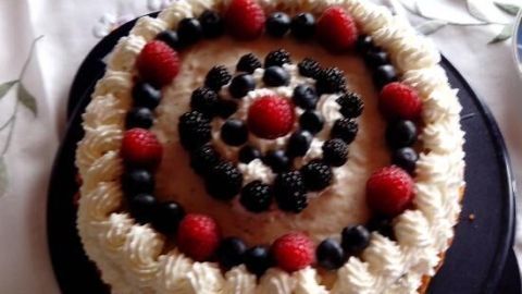 Eine dekorative Torte mit Brombeeren und Sahnefüllung wird auf einem Tisch serviert, umgeben von Geschirr.