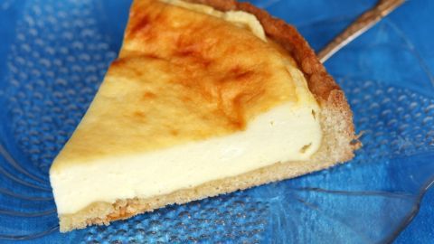 Ein Stück Käsekuchen liegt auf einem blauen Teller, während ein Löffel danebensteht, bereit zum Servieren.
